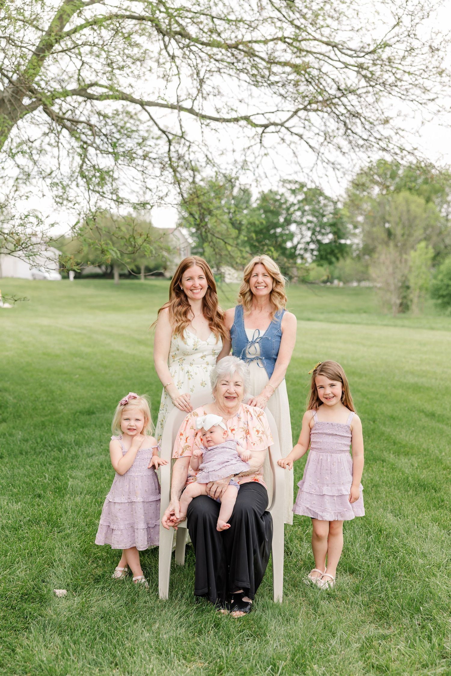 Multi-generational family portrait with five females outdoors on green grass under a tree in spring.