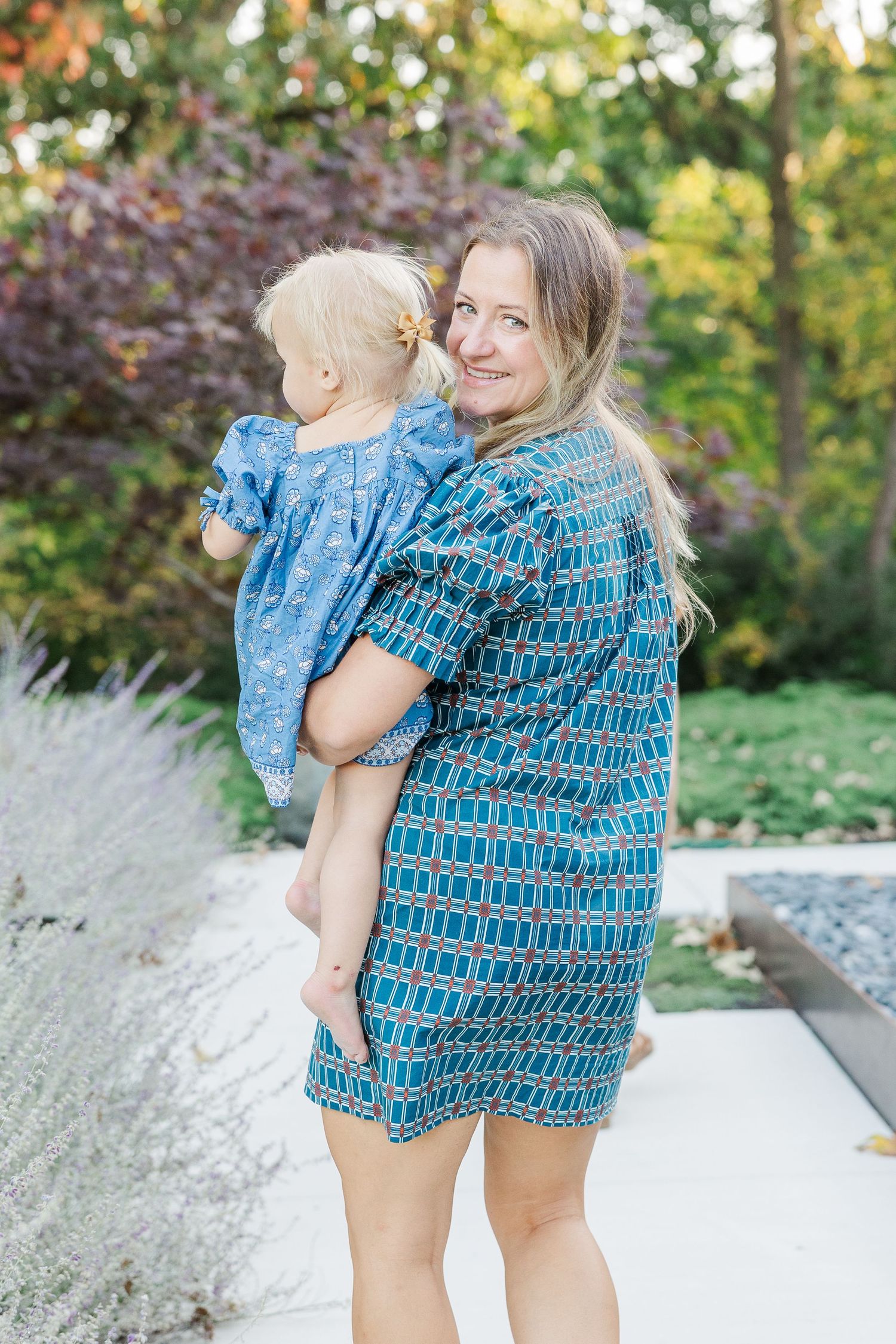 Mother and baby in matching blue patterned outfits share sweet moments outdoors in a garden setting.