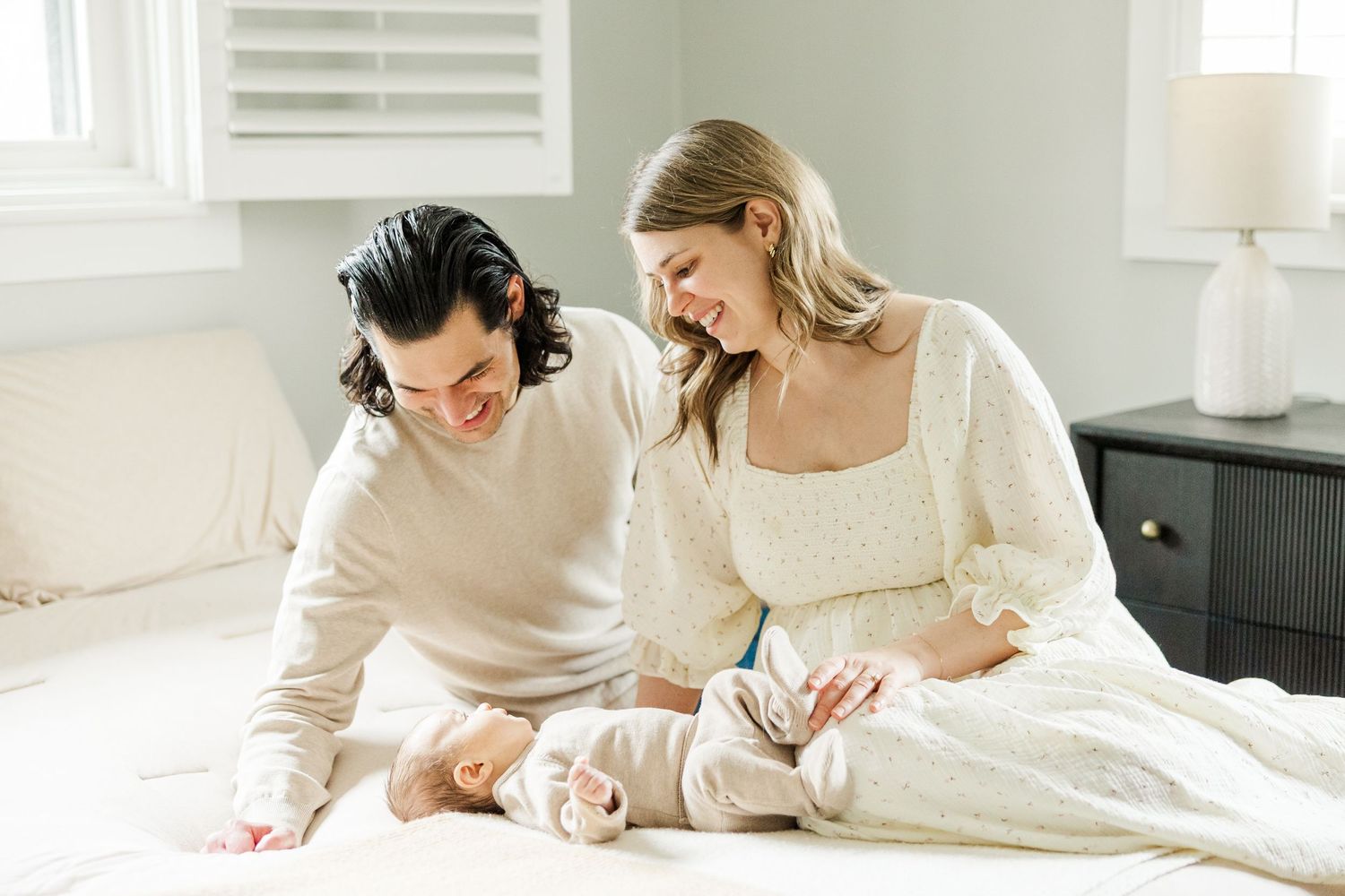 Parents sitting on their bed smiling down at their newborn baby during an in-home lifestyle newborn photography session in Palatine Illinois