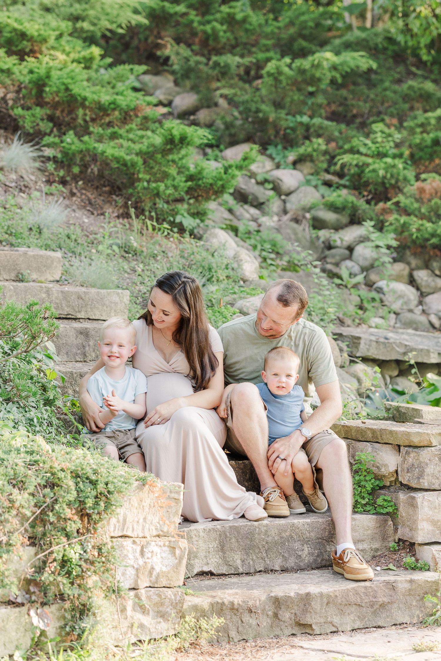 A family sits together on rustic stone steps surrounded by lush greenery in a peaceful outdoor setting.