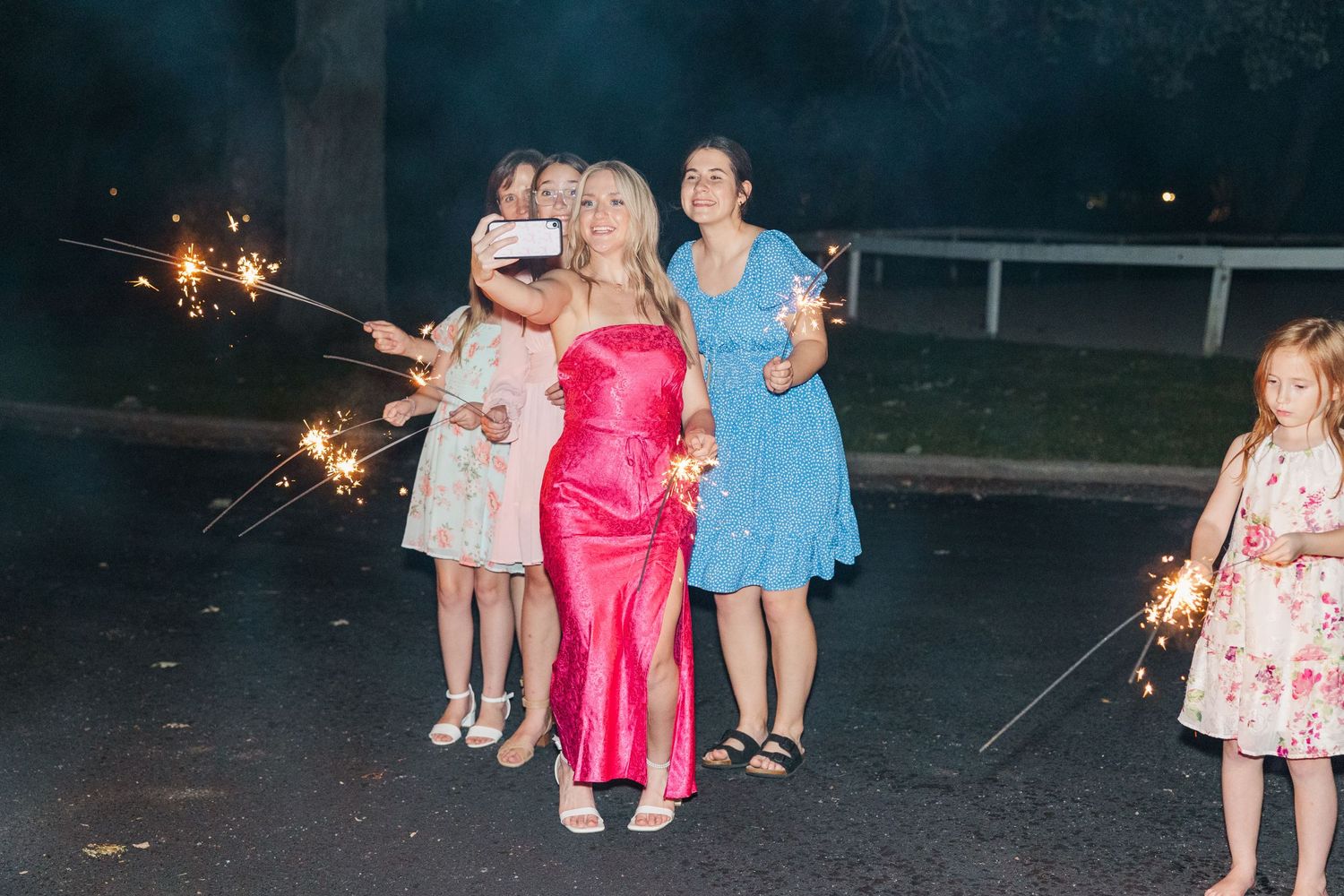 Celebration guests enjoy sparklers outdoors while wearing formal dresses.