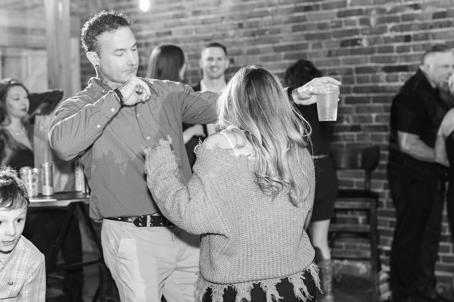 Black and white photo of wedding guests dancing at a casual reception.