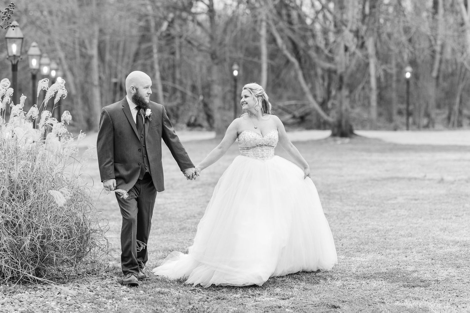Black and white wedding photo of a couple walking together in a park setting.