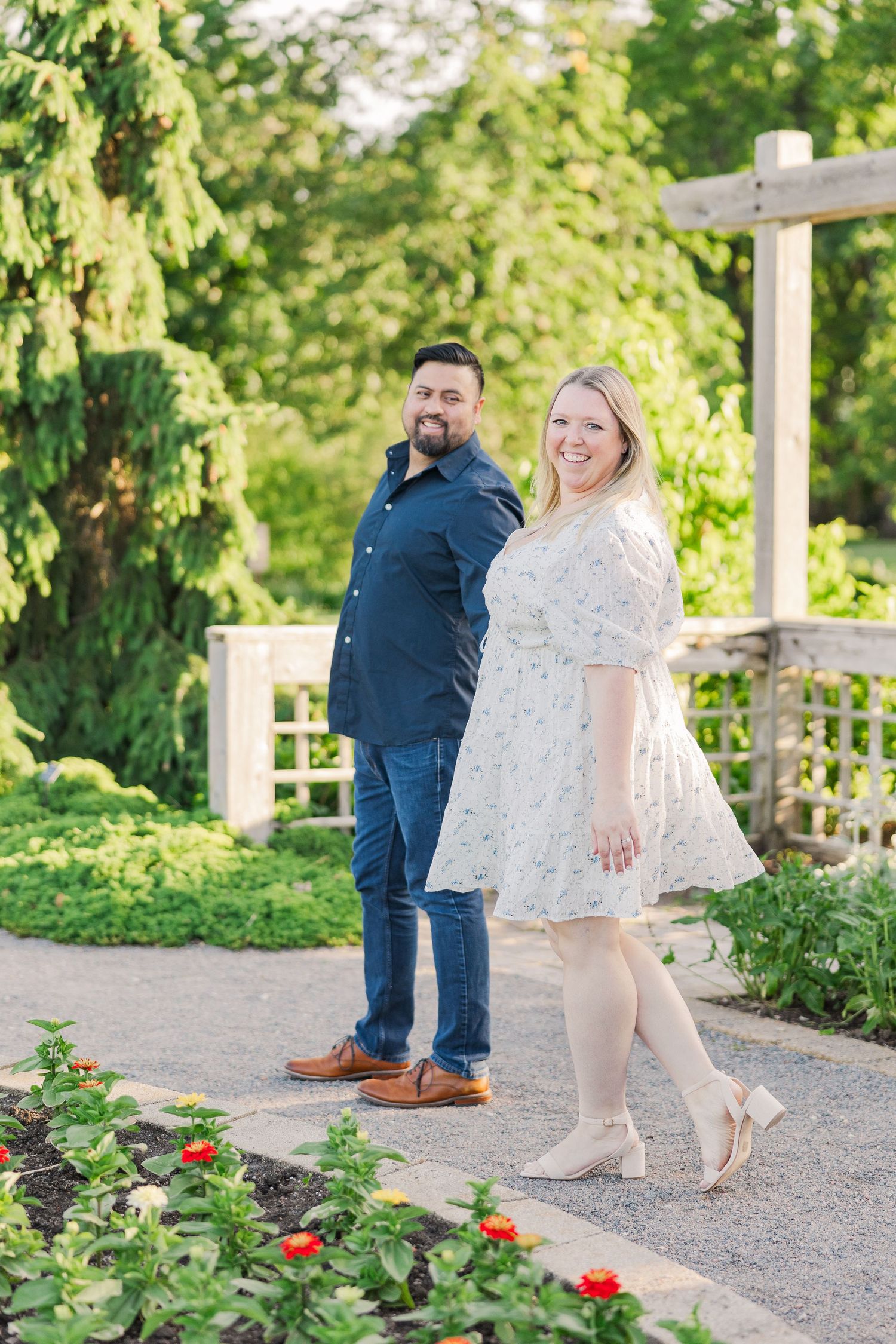 A couple poses playfully on a garden path with colorful flowers and greenery.