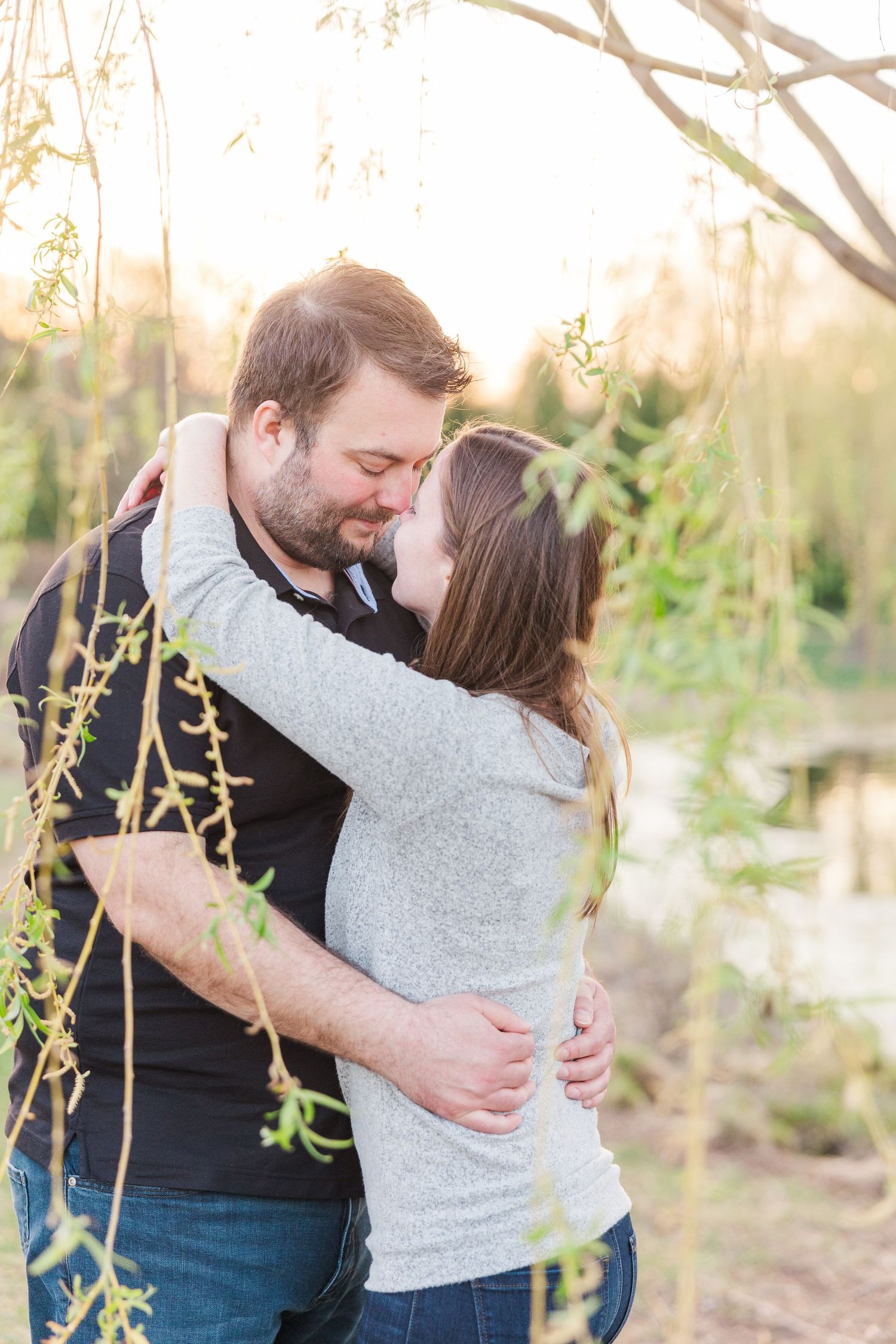 Tender moment between couple embracing among spring branches at golden hour.