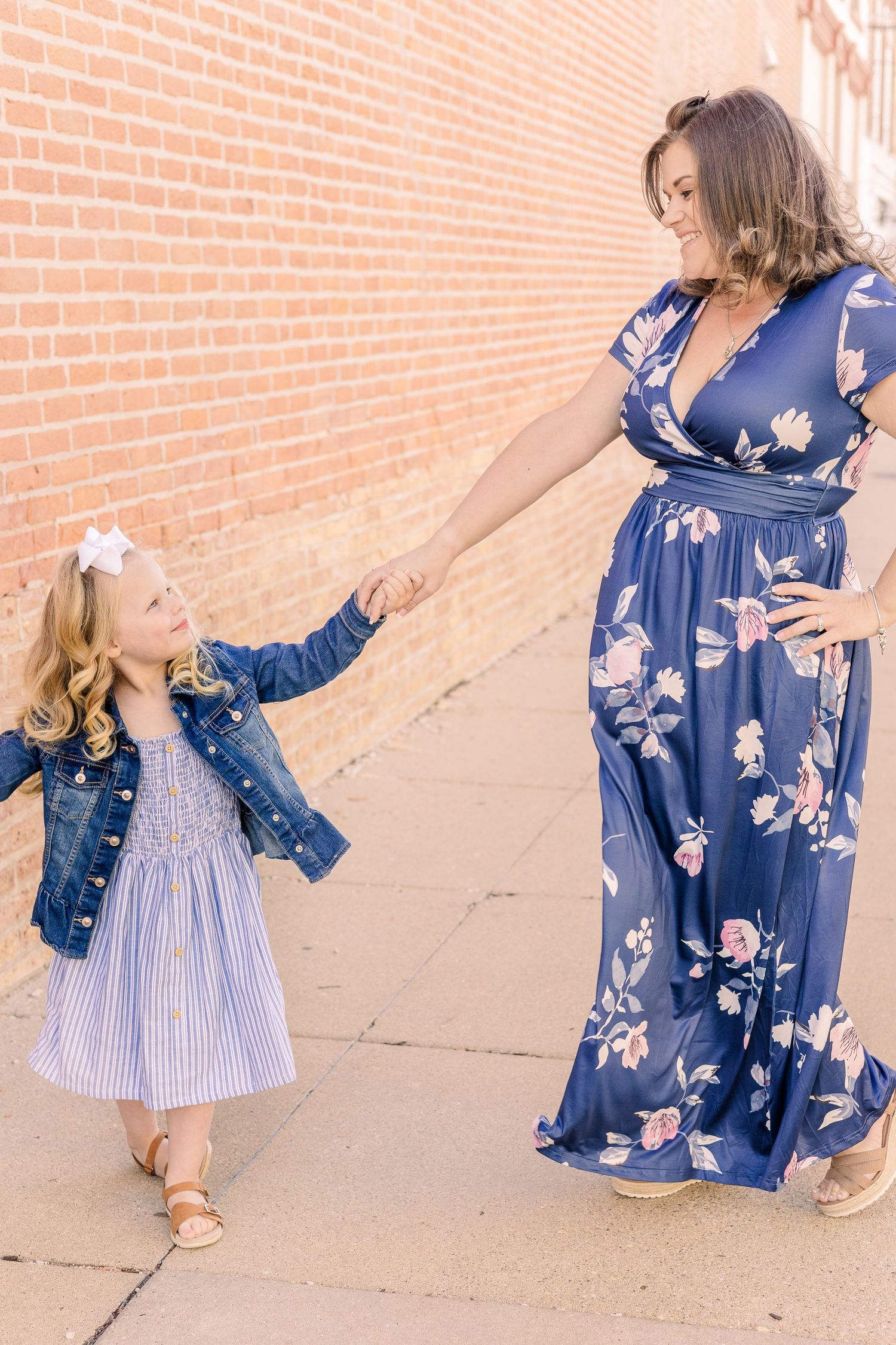 Two people in blue dresses share a playful moment while walking along a brick wall.