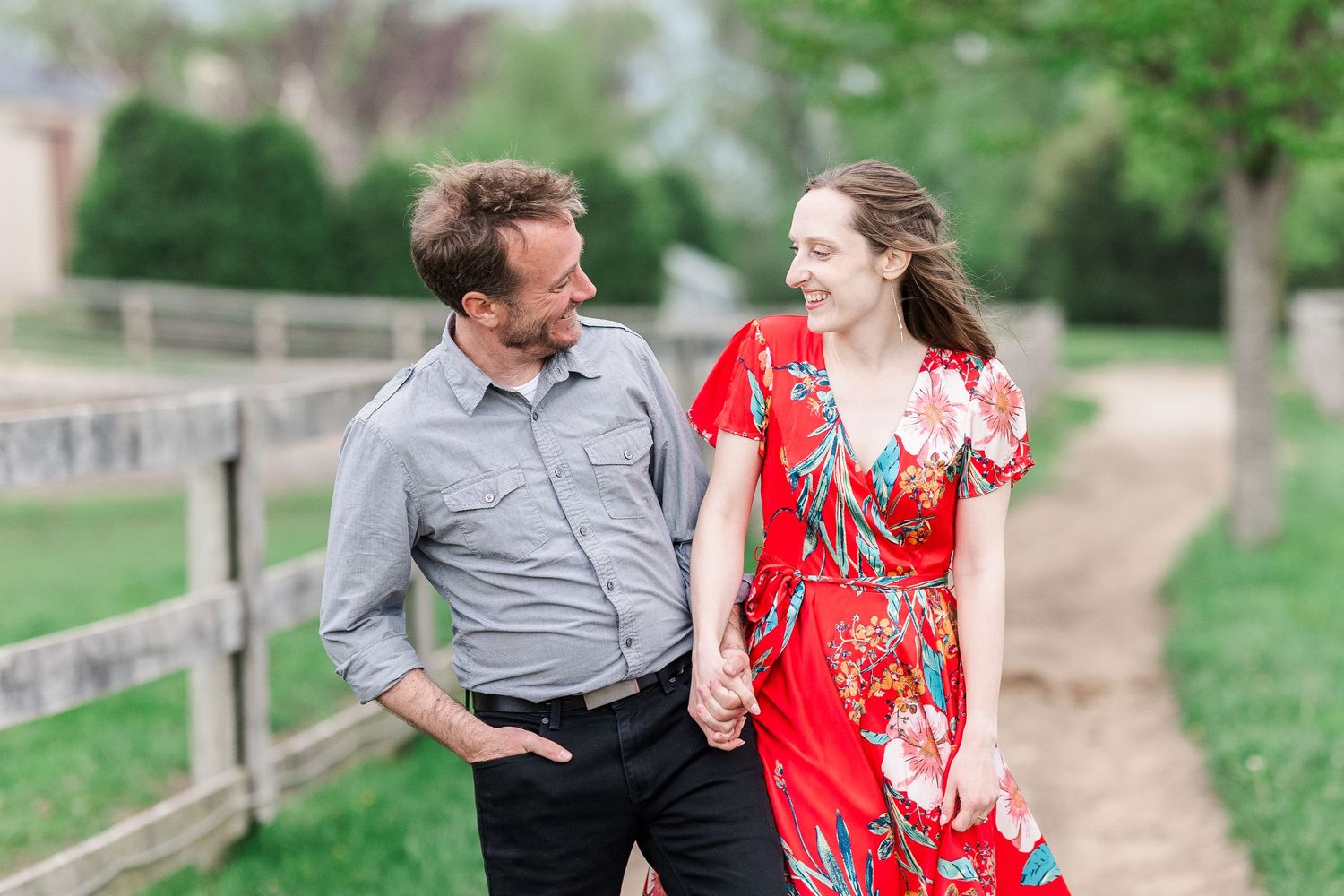 A couple shares a loving moment on a dirt path lined with wooden fences and spring greenery.