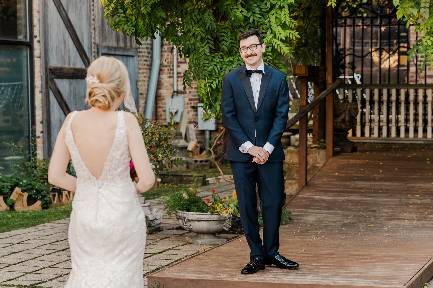 Wedding first look scene in garden courtyard with navy suited groom waiting for bride.