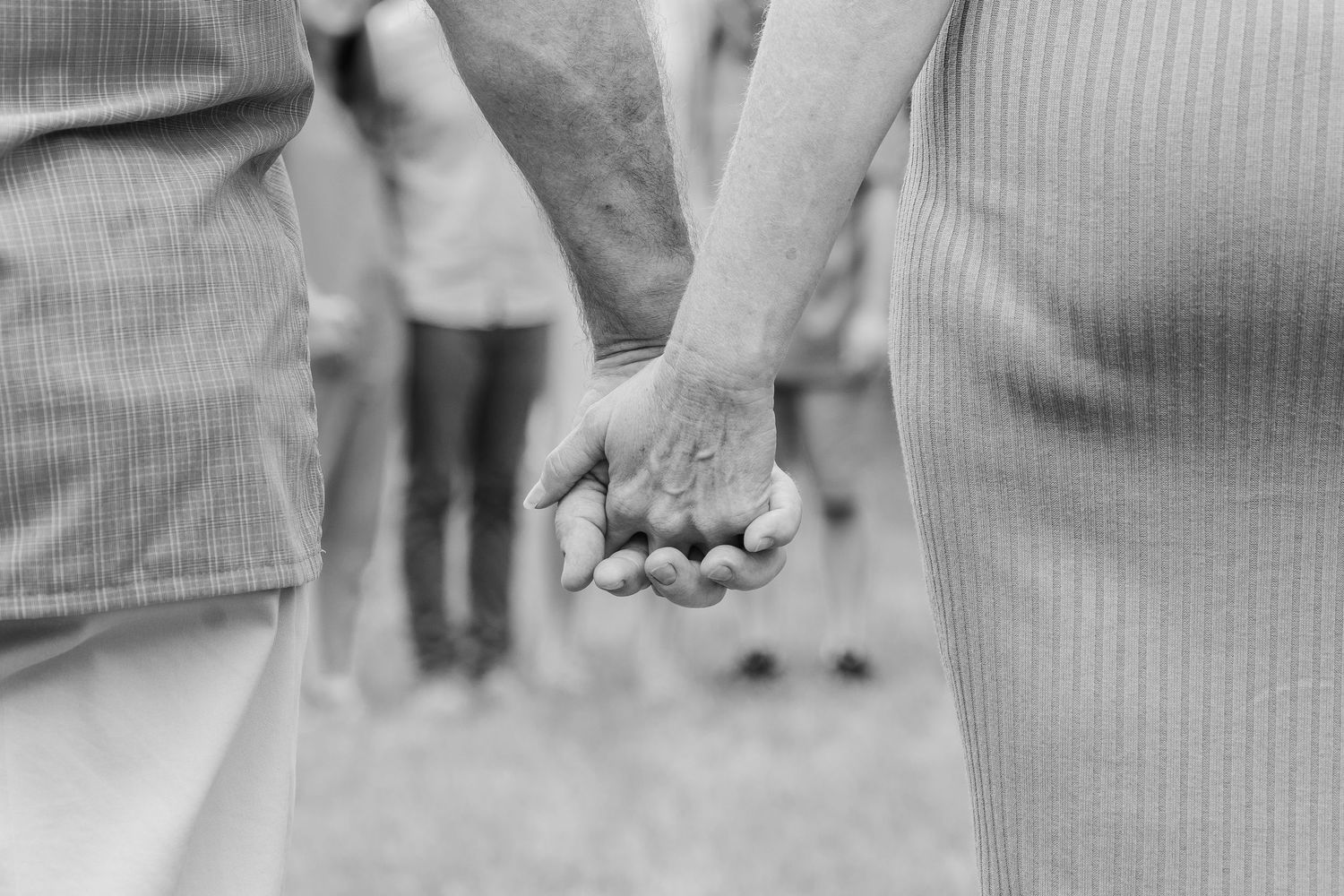 A close-up black and white shot of two people holding hands.