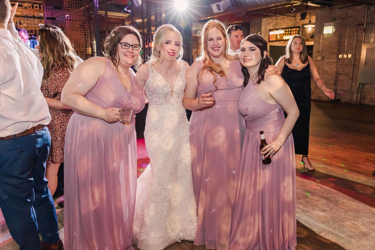 Group of women in pink dresses posing during wedding celebration in rustic venue.