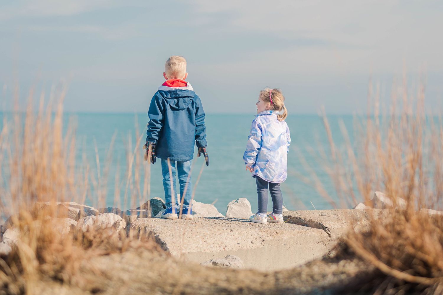 Two figures stand together on a rocky outcrop overlooking a serene lake on a sunny day.