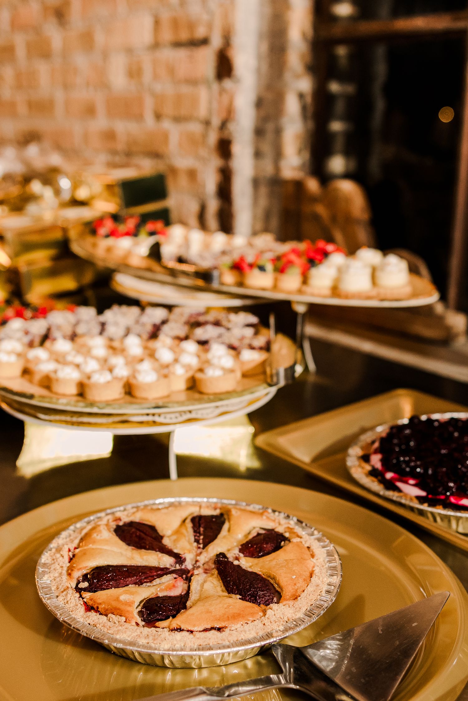 Wedding dessert spread featuring fruit pies and white pastries on elegant cake stands.