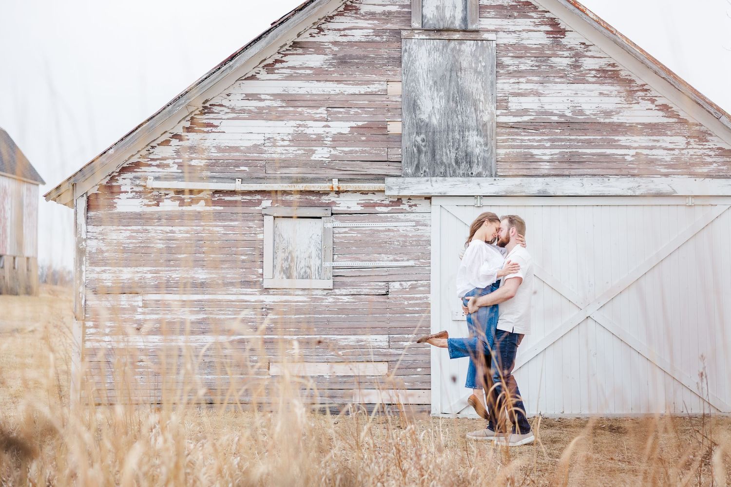 Couple embracing by rustic barn during pregnancy announcement photos in Cary, Illinois
