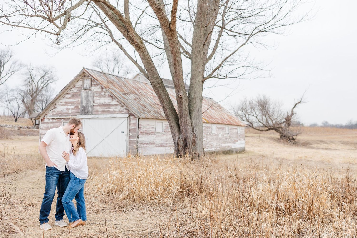 Couple walking by rustic barn during pregnancy announcement photos in Cary, Illinois