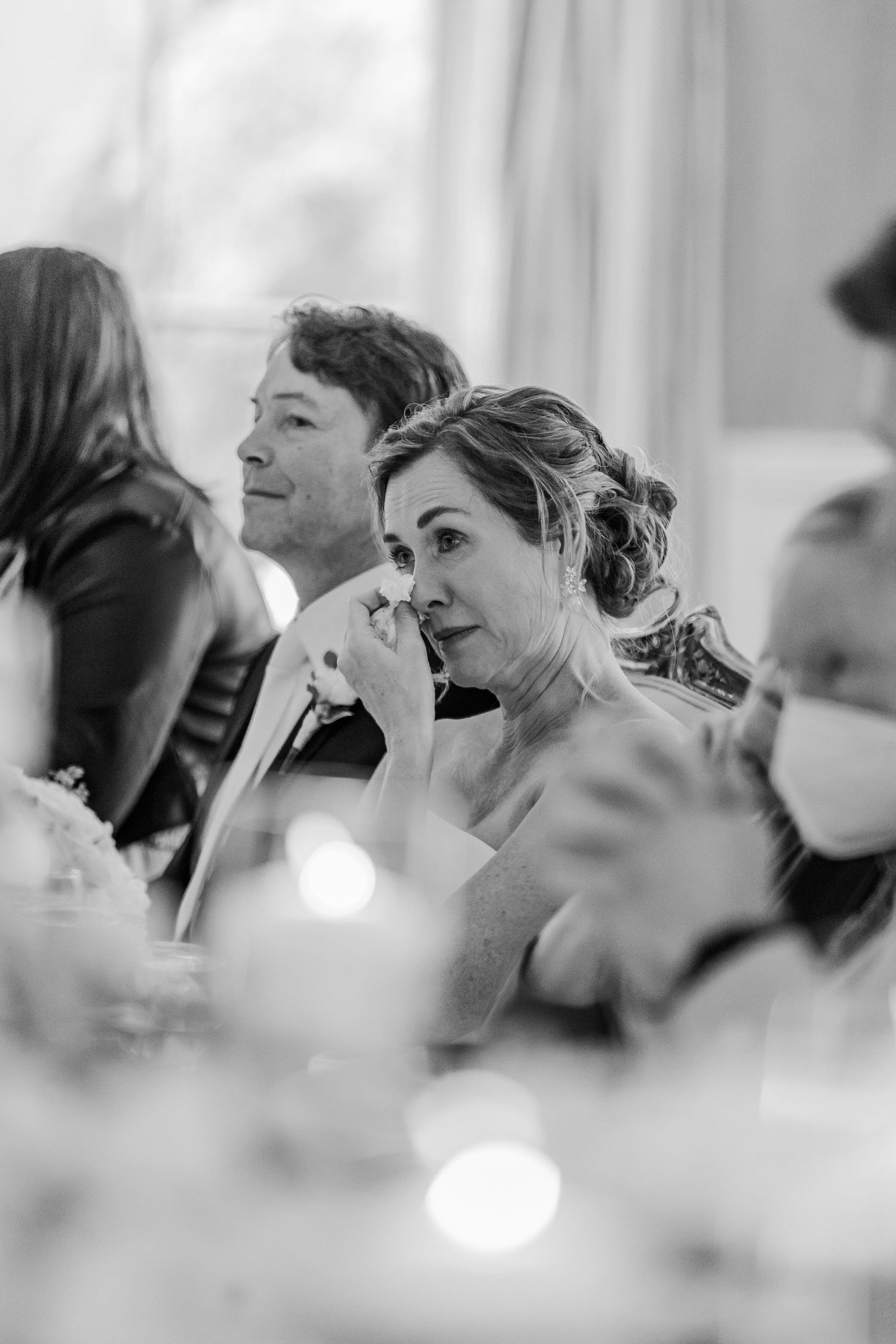 Black and white candid photo of wedding reception guests during emotional moment.