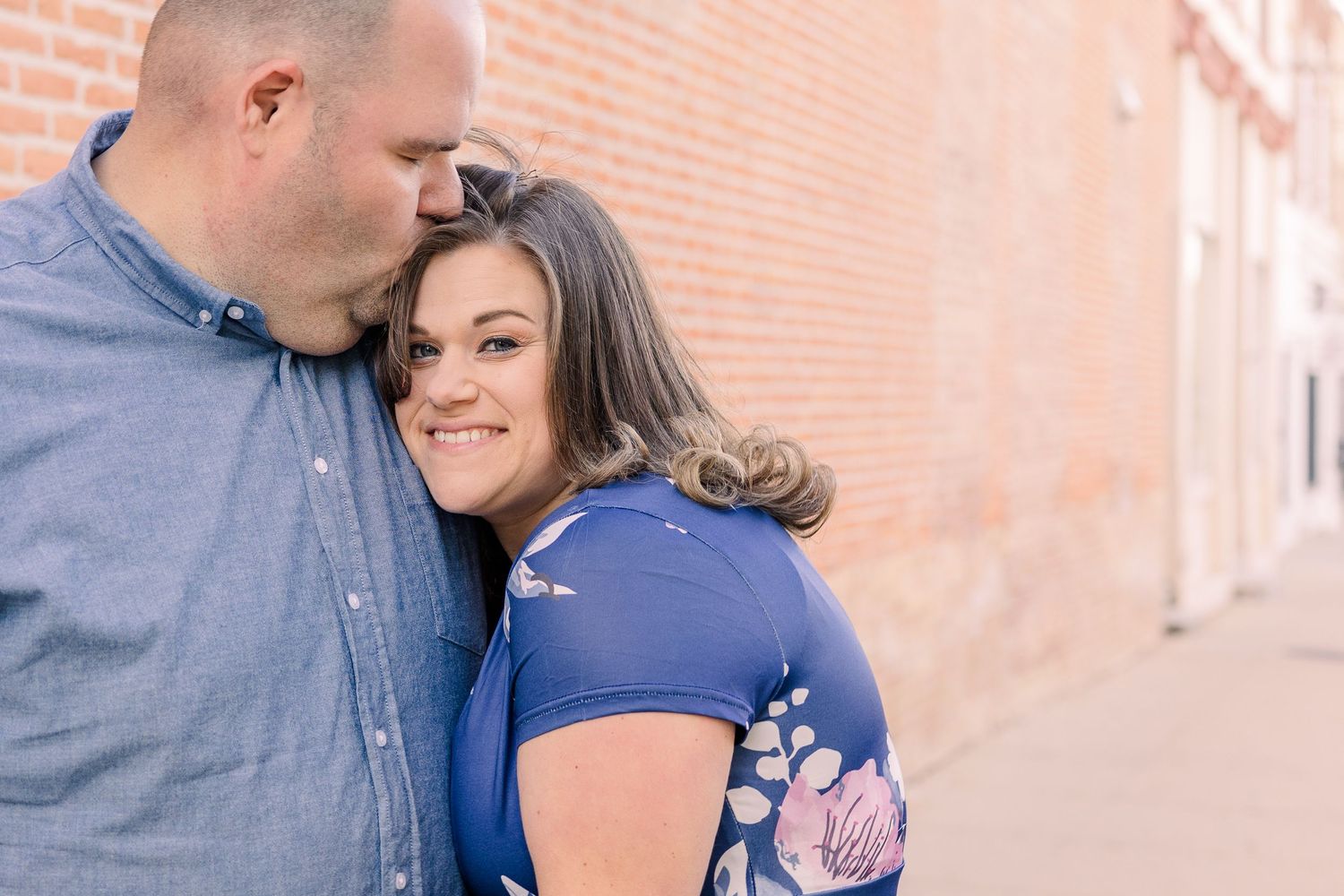 Close up of affectionate couple posing against orange brick wall.