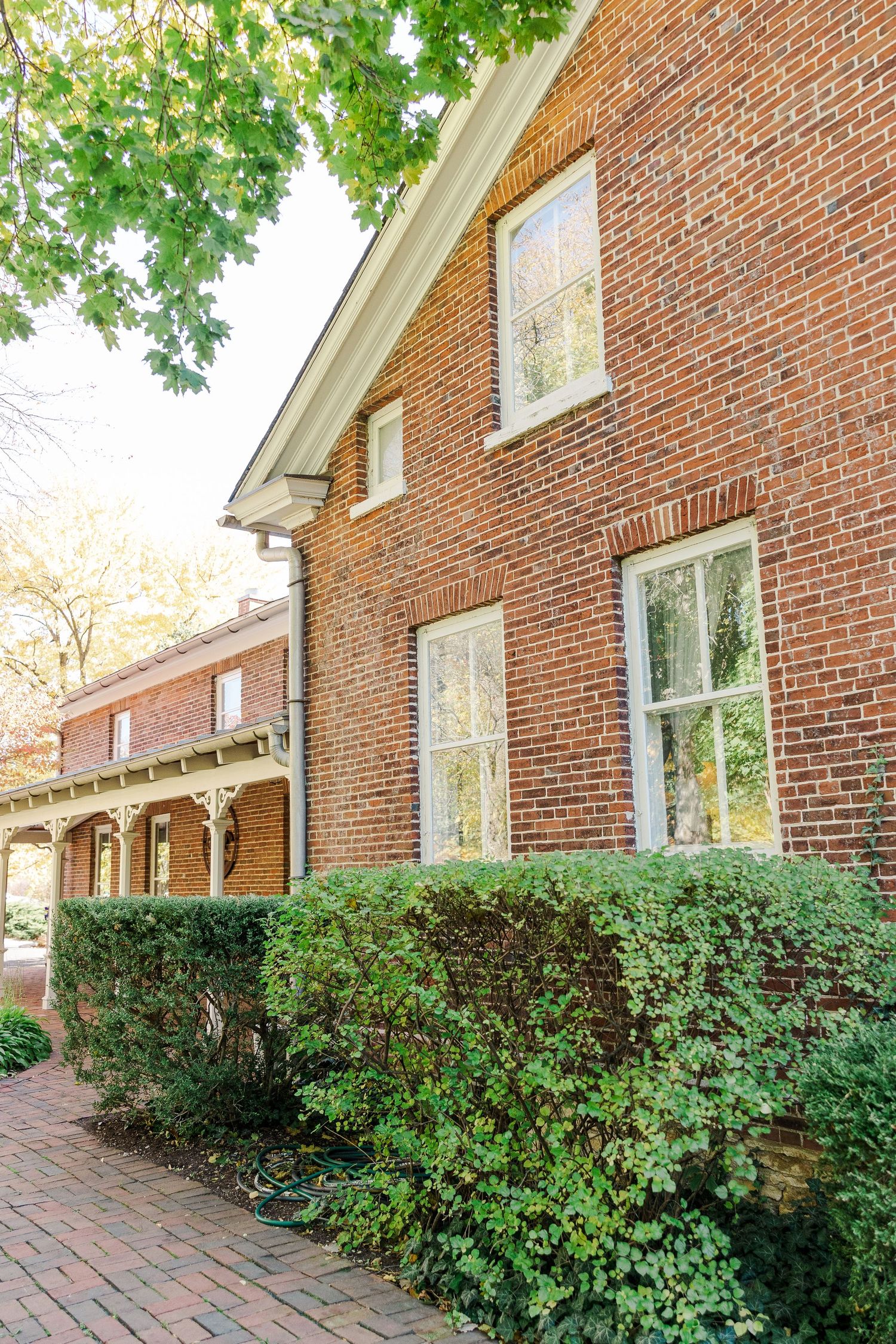 Exterior of historic brick building with white trim windows and lush green landscaping.
