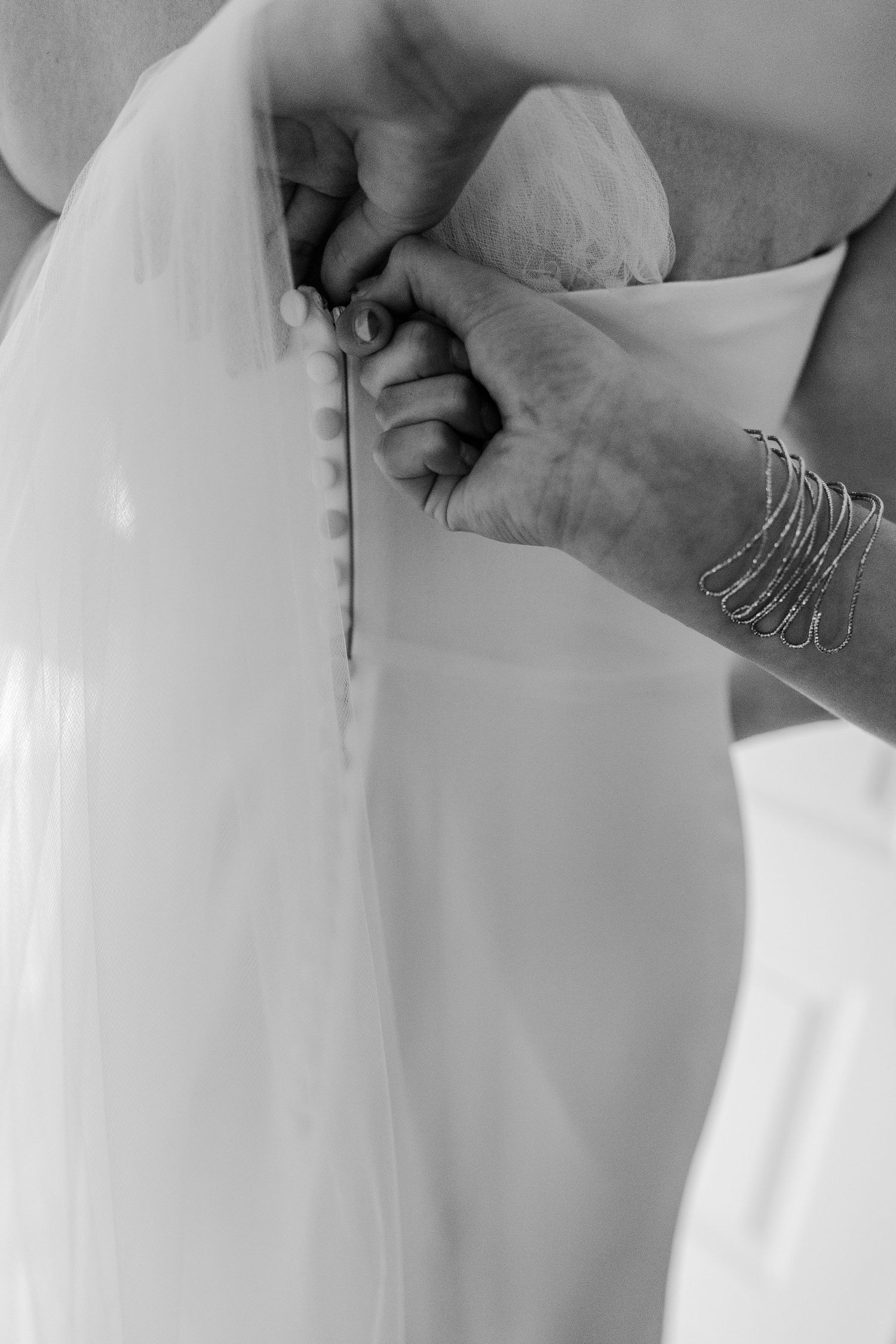 Close-up black and white shot of hands fastening buttons on a wedding dress.