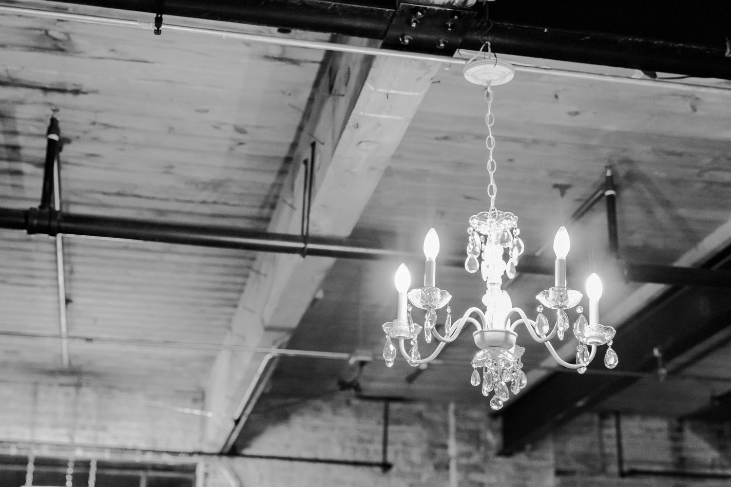 Crystal chandelier hangs from an industrial ceiling in black and white.
