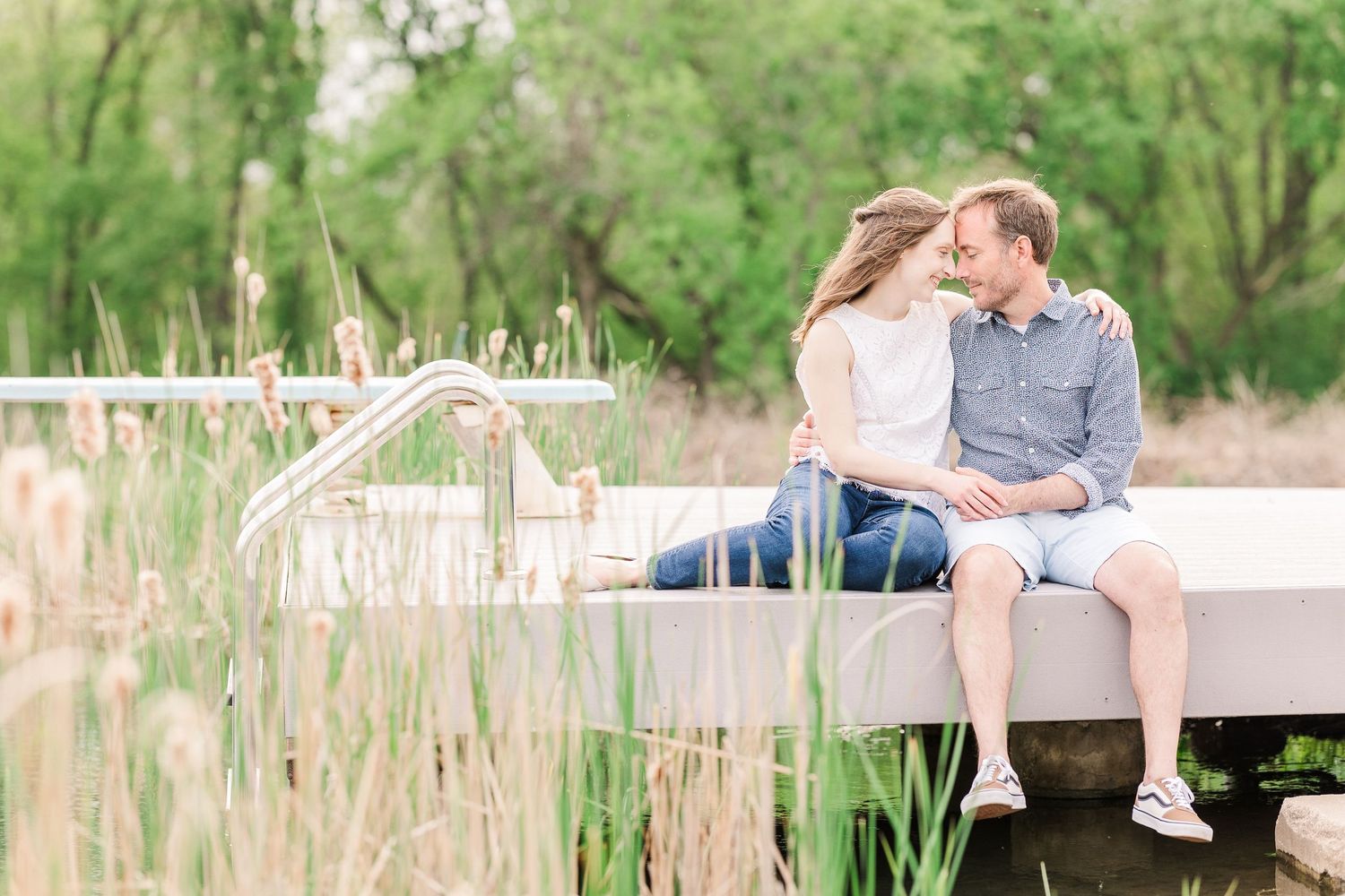 Couple sitting close together on wooden dock overlooking peaceful pond.