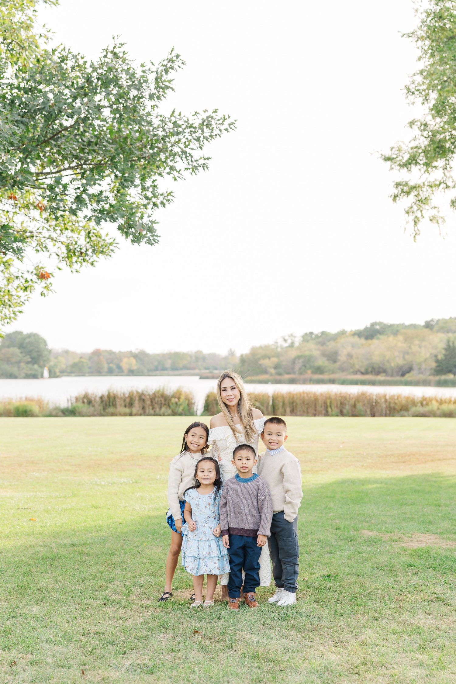 Children sit together in a grassy field on an autumn day with golden sunlight and trees in the background. Busse Woods