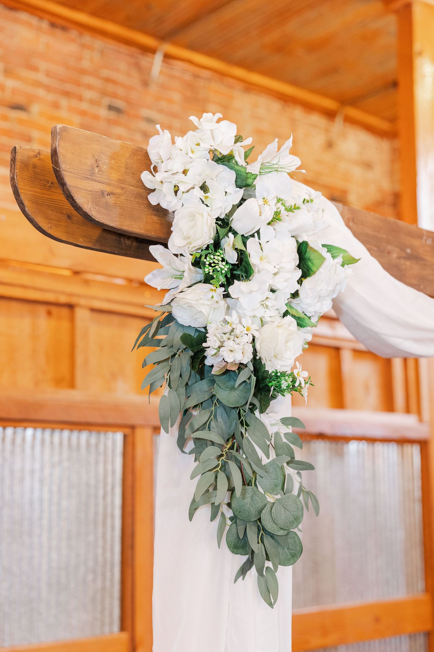 White floral arrangement with cascading eucalyptus leaves on wooden ceremony backdrop.