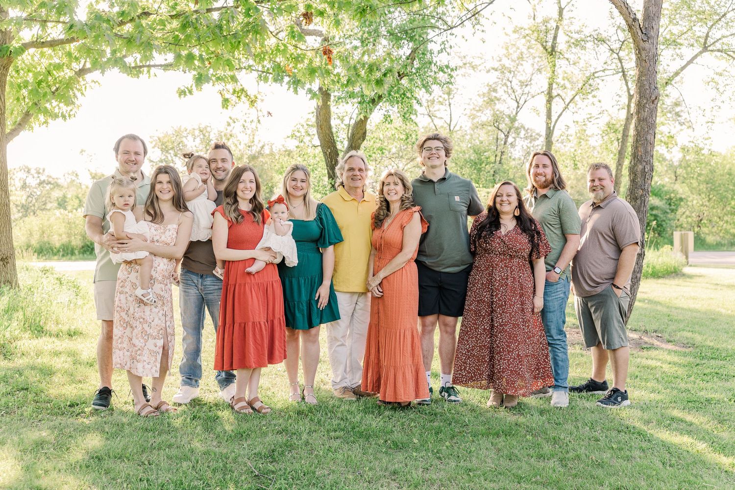 Family group photo with members dressed in coordinating spring colors standing under trees.