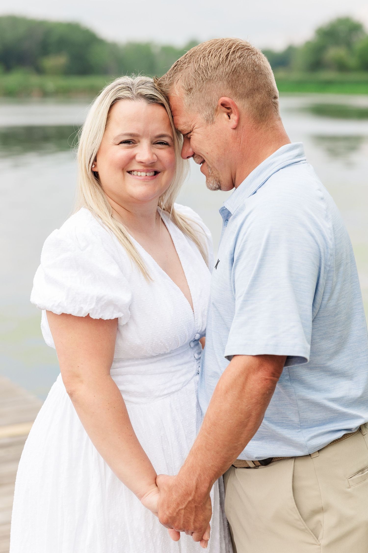 Happy couple shares intimate moment on wooden dock with lake view behind them.
