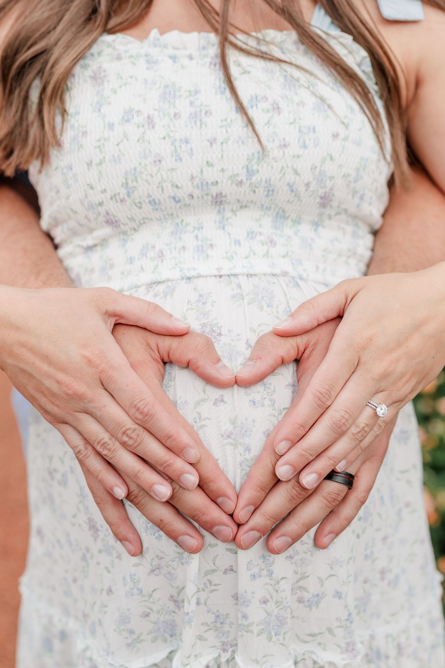 Close-up maternity detail photo of expecting parents making a heart over baby bump