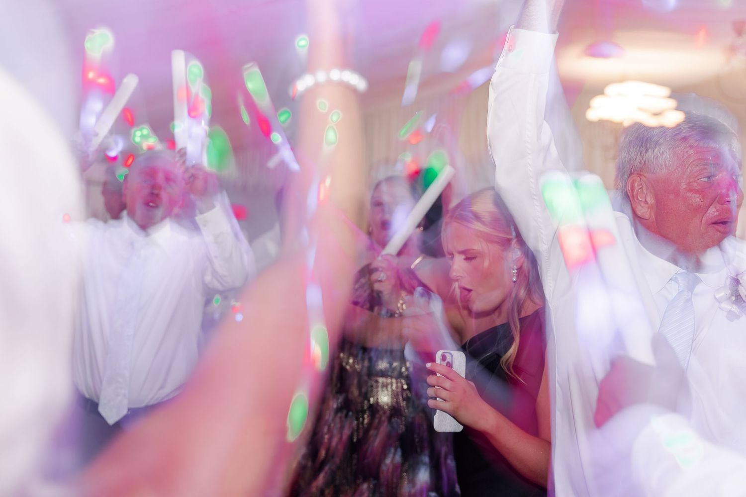 Wedding guests dancing with colorful glow sticks during a lively reception celebration.