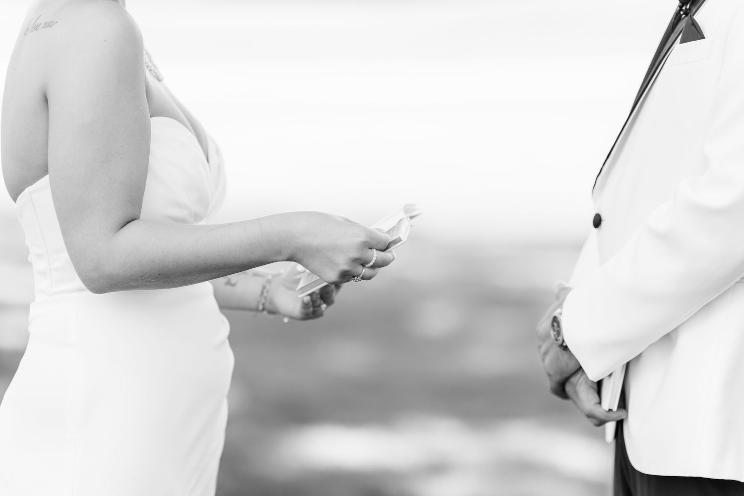 Bride reading wedding vows from paper during outdoor ceremony in black and white photo.