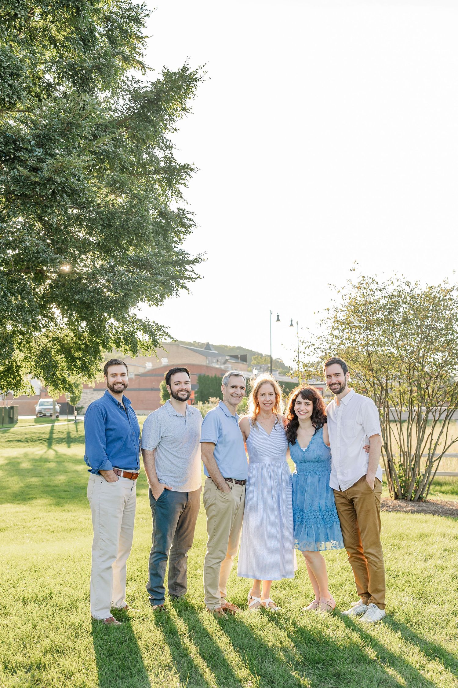 Group of six adults smiling together outdoors in sunny green park.