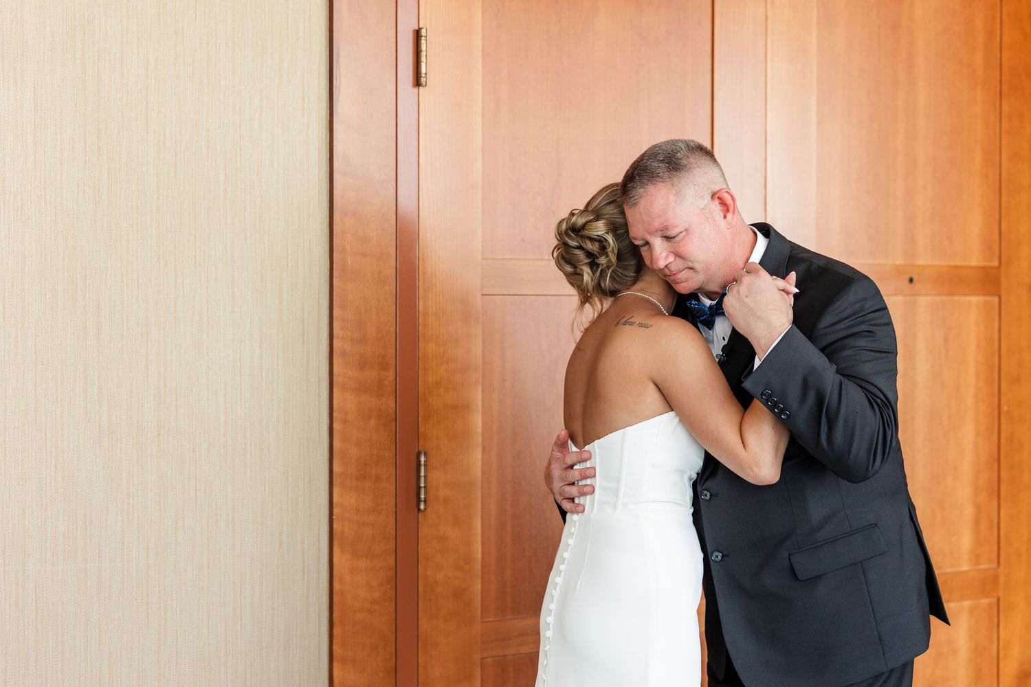 Emotional first look moment as groom embraces bride in white gown against wooden doors.