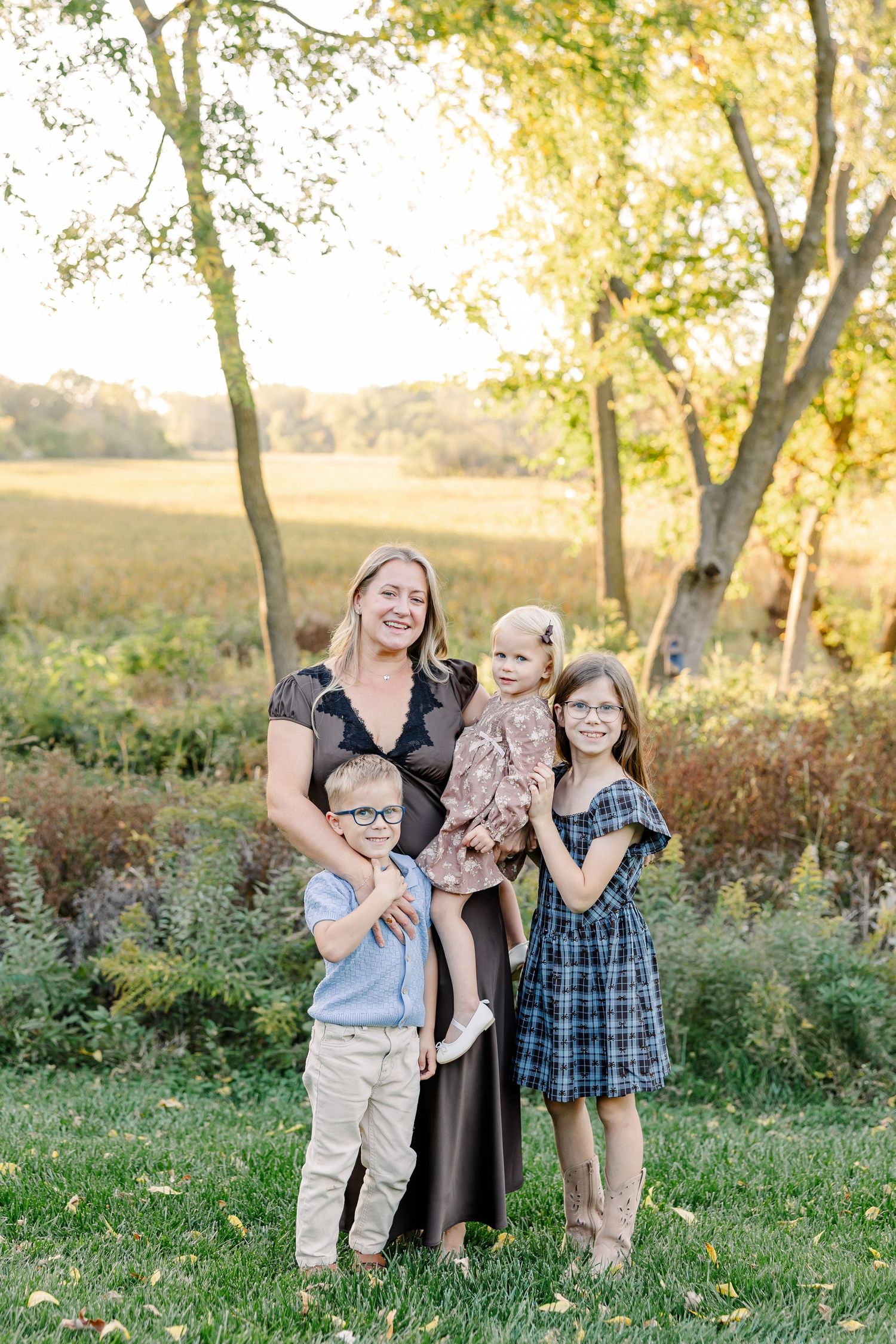 Mom with her three children beneath glowing backyard trees during fall portraits in St. Charles, IL.