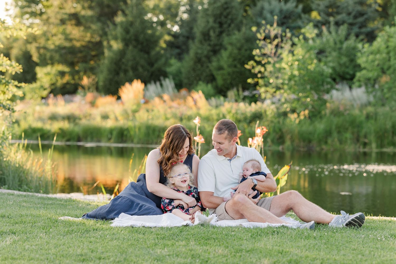 Hilary and Andrew looking down at their children during their outdoor family session by the pond.