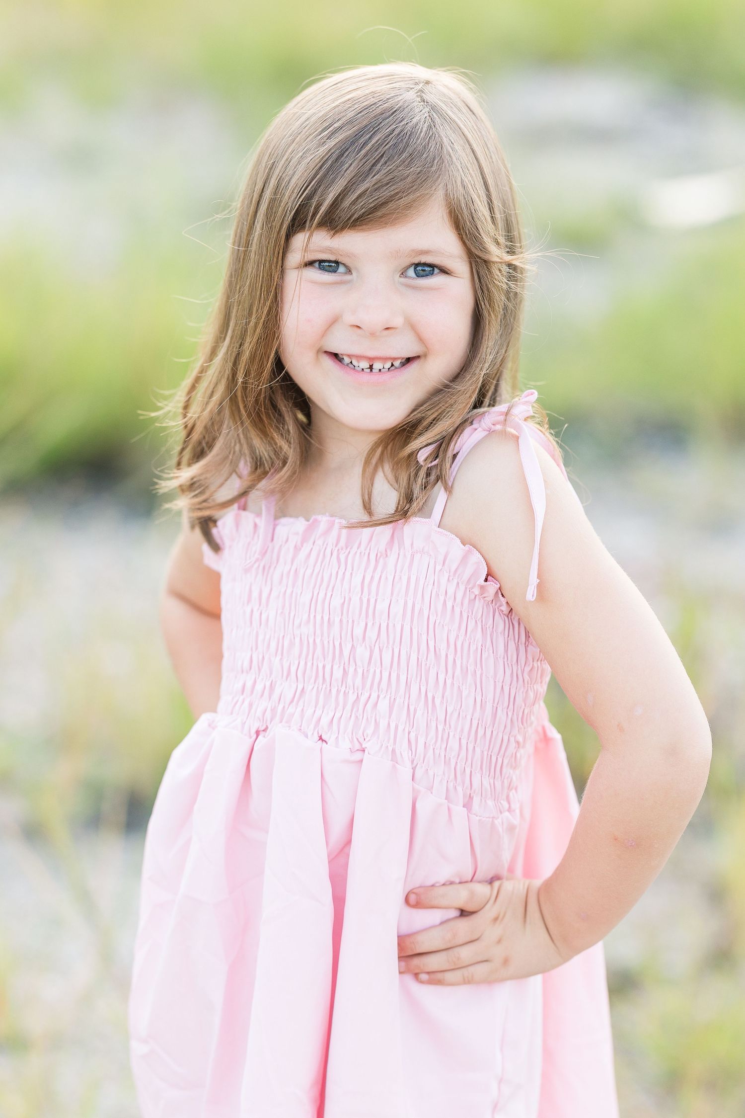A child in a pink ruffled dress stands outdoors in a natural setting on a sunny day.