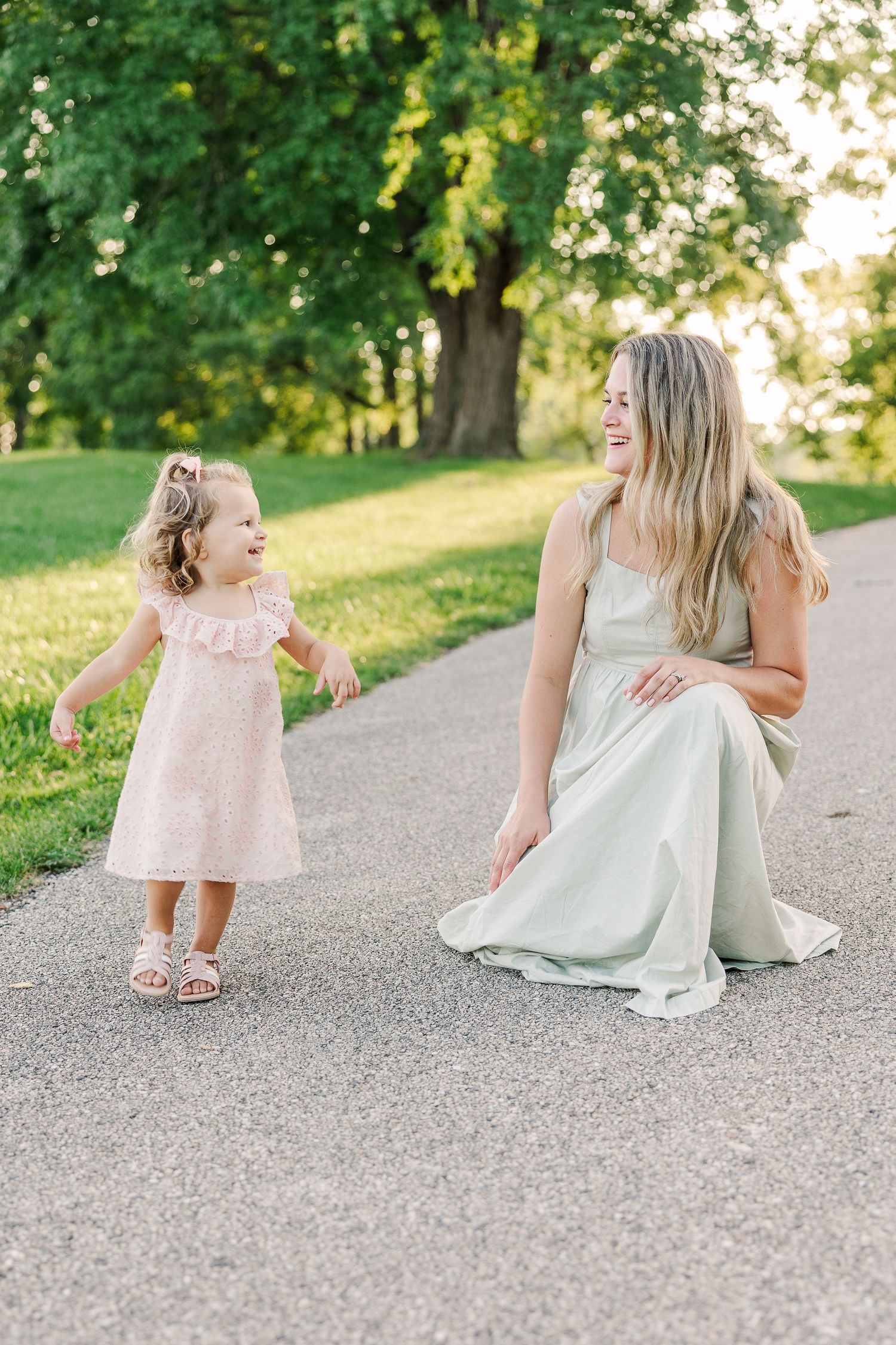 A tender moment between a woman and small child in dresses on a peaceful park path.