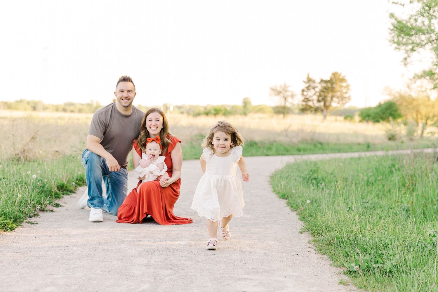 A playful family photo session on a path with a child running ahead in a white dress.