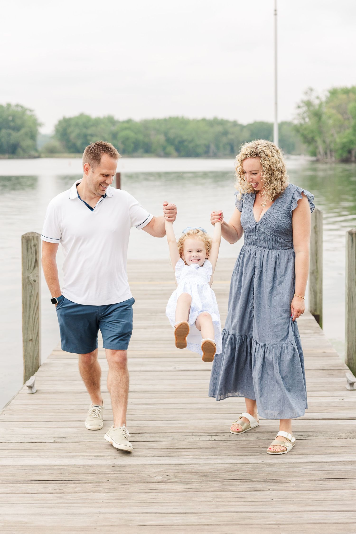 A family enjoys a playful moment together on a lakeside dock on a sunny afternoon.