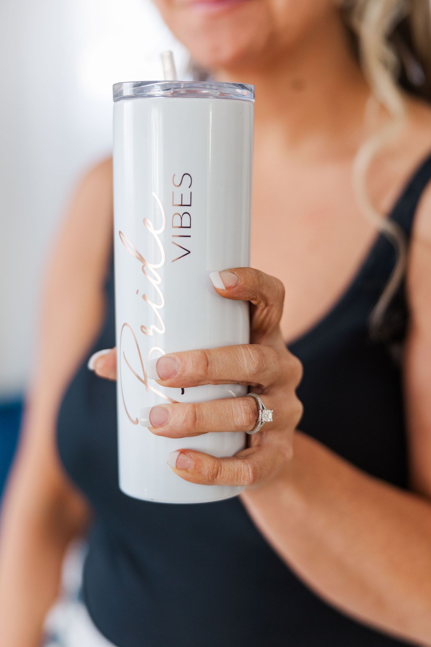 A white insulated tumbler with the word 'vibes' being held by a hand with an engagement ring.