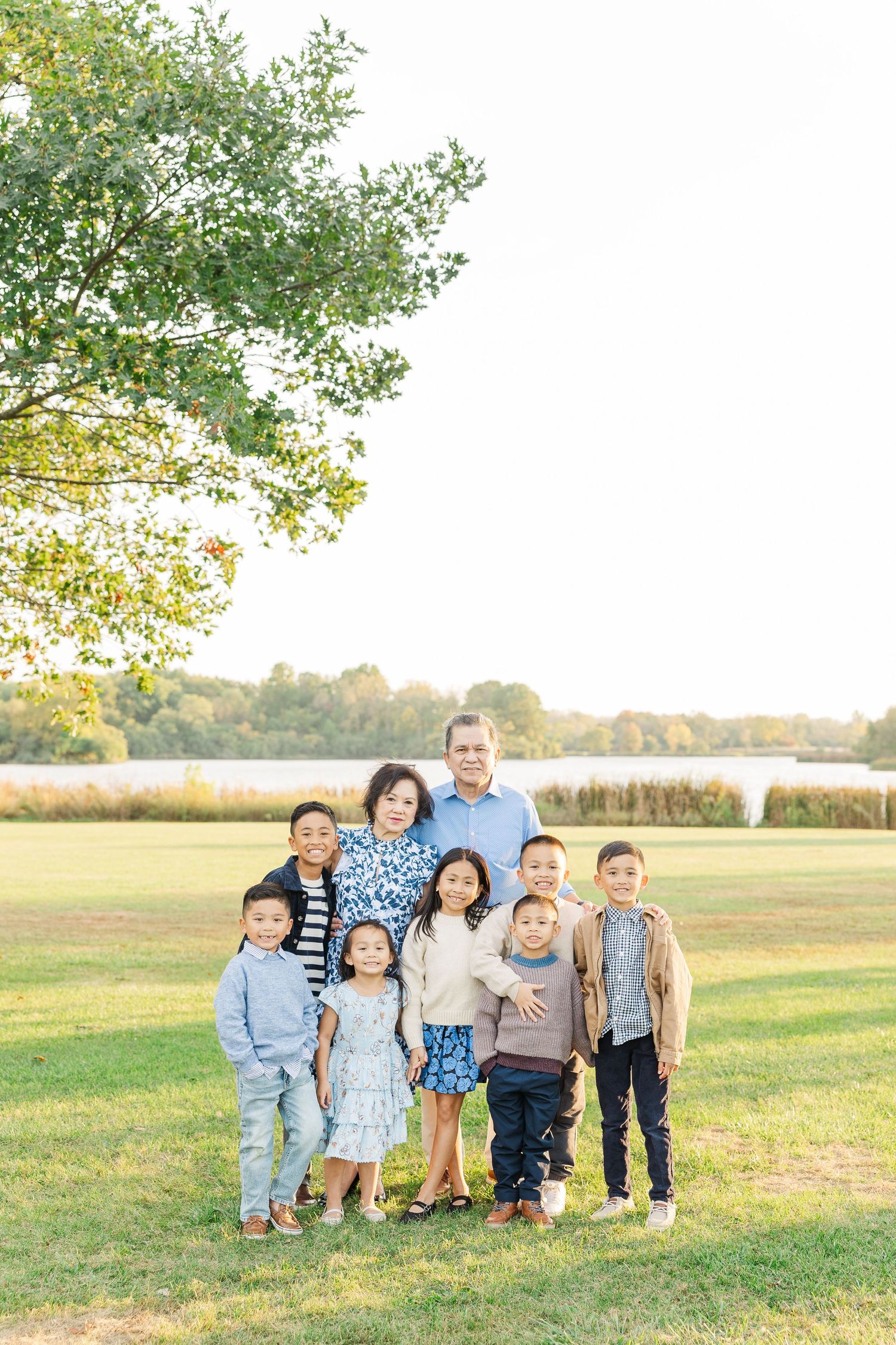 A group sits together on grassy field during golden hour with trees and autumn foliage in background. Busse Woods