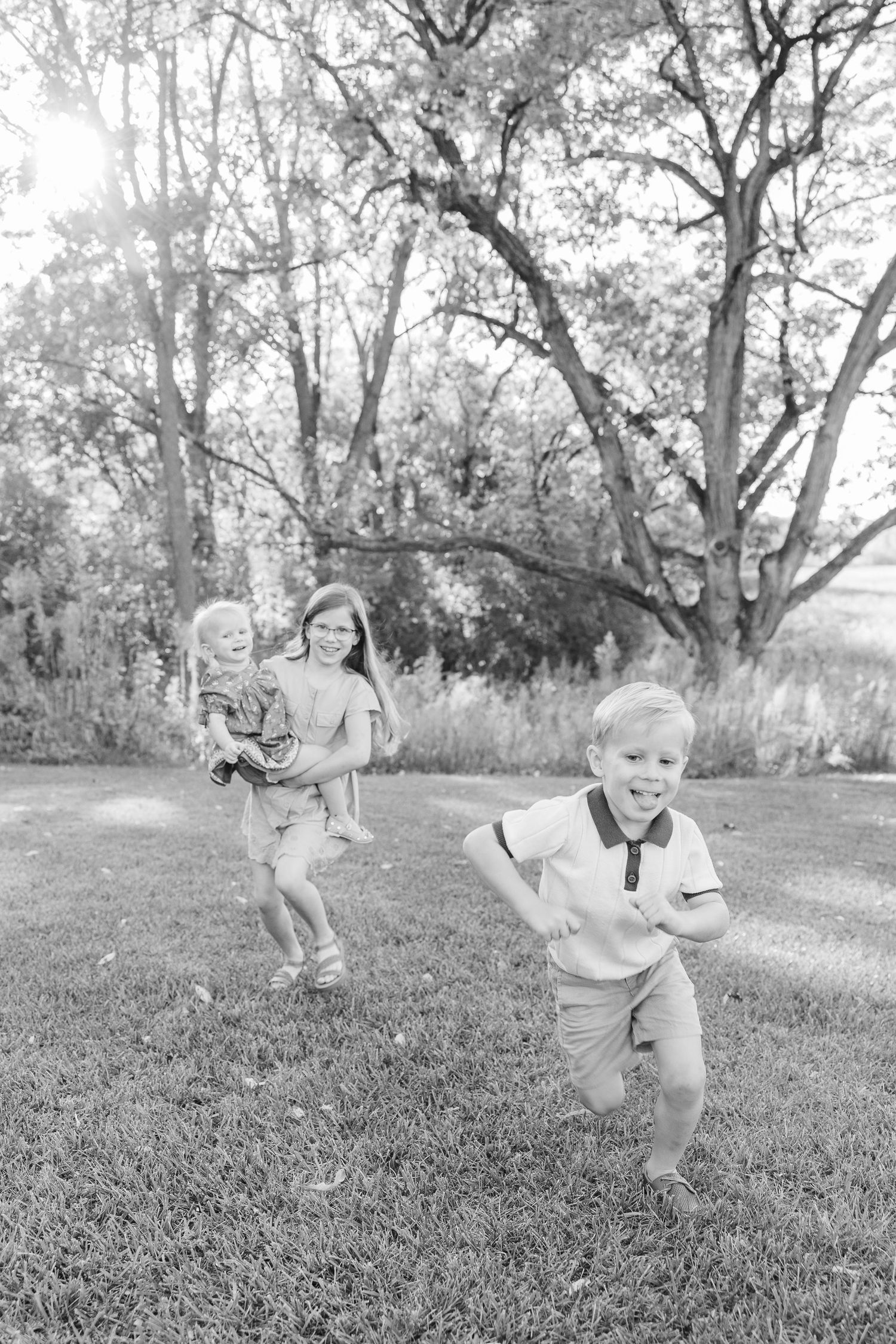 Black and white photo of children running and playing together on grass with trees in background.