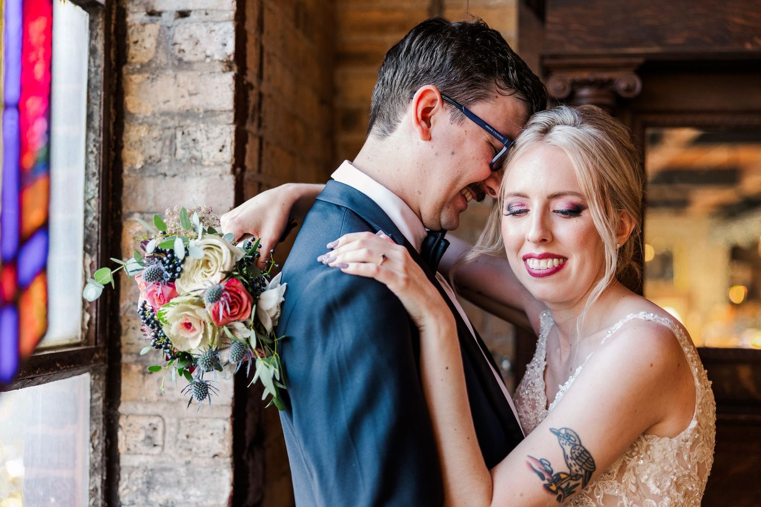 An intimate moment between newlyweds with colorful stained glass window in background.