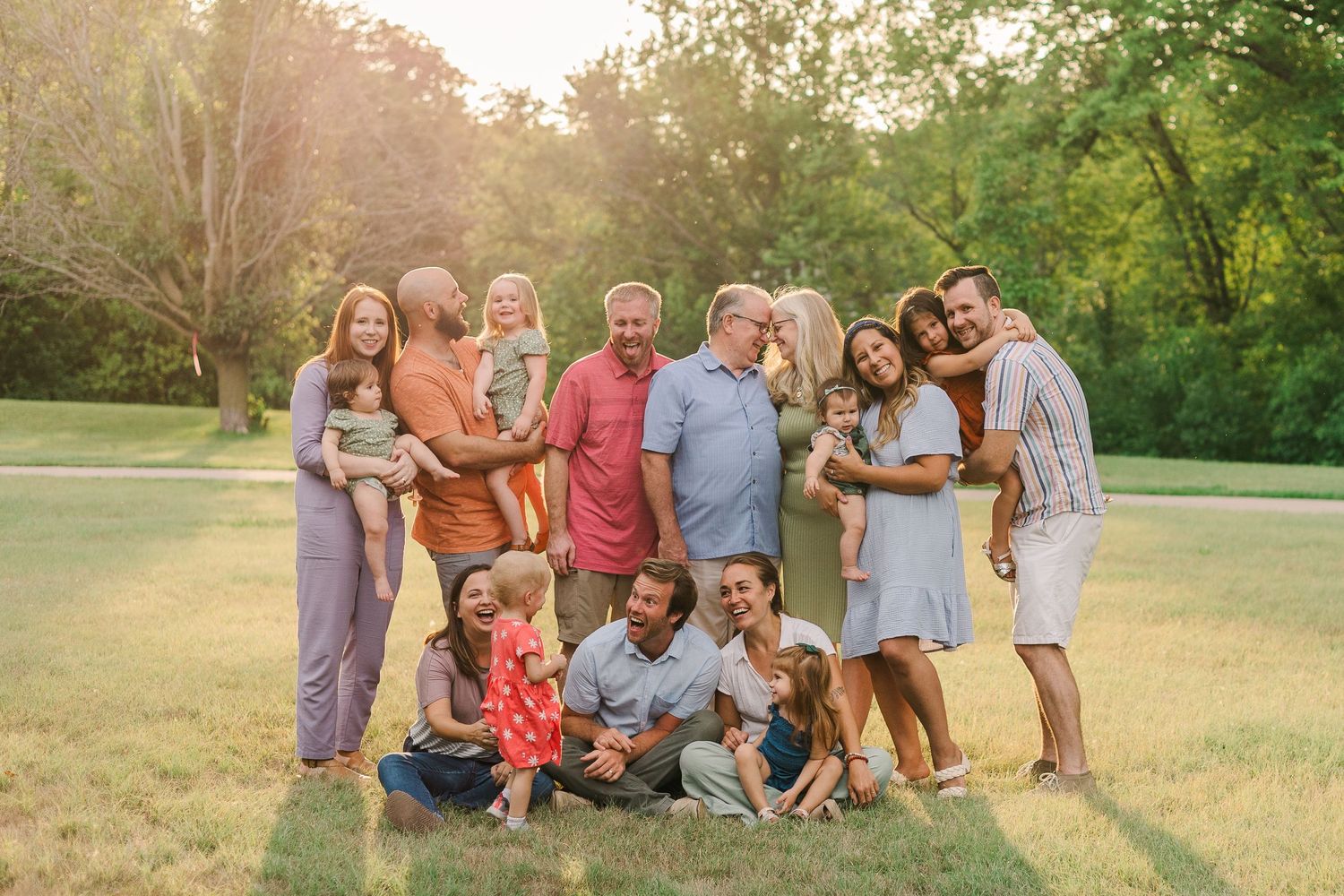 A large multi-generational family poses together for a portrait during golden hour in a grassy field.