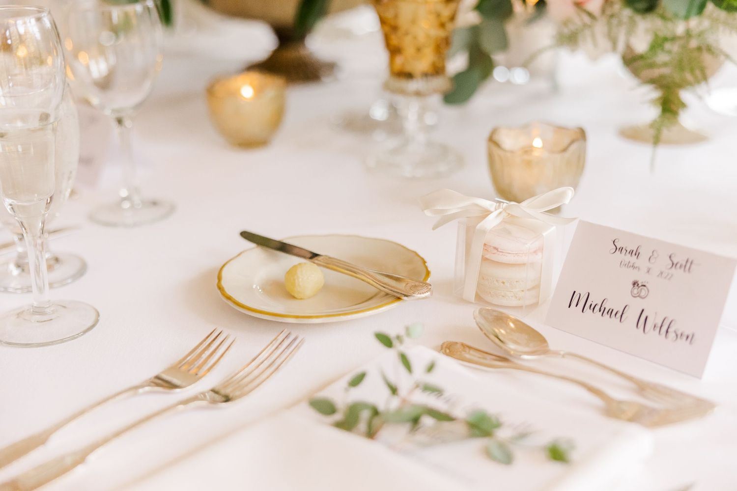 Gold place setting with white plate, elegant flatware, and name card decorated with greenery.