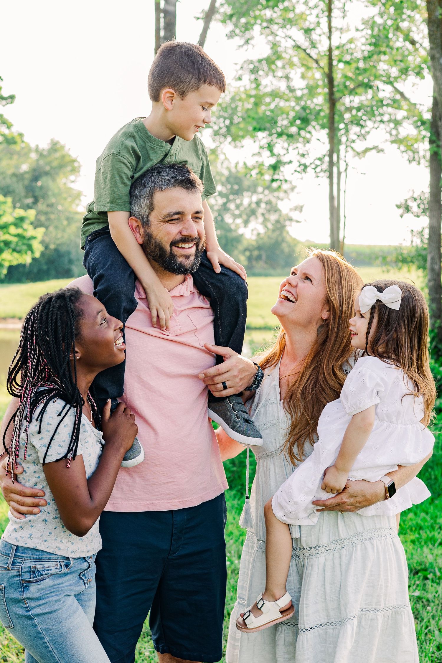 A joyful family shares laughter while posing together in a sunlit park setting.