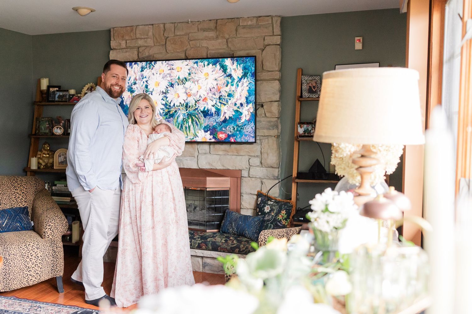 Couple smiling together in a cozy living room with a stone fireplace and colorful floral artwork above it.