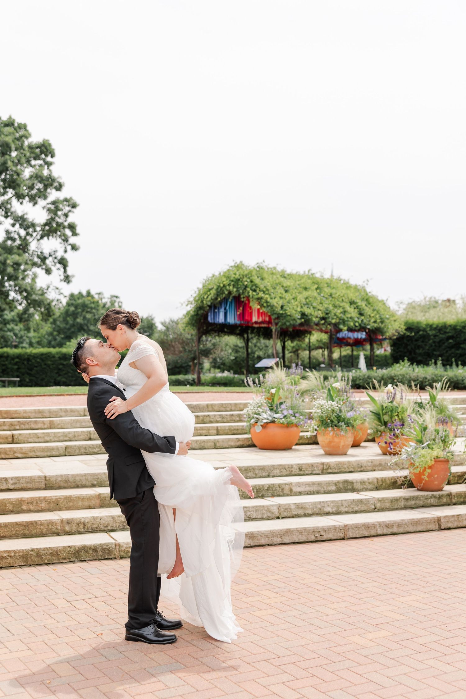 Rafael lifting Monika as they kiss near the garden steps and summer flower displays at Cantigny Park.