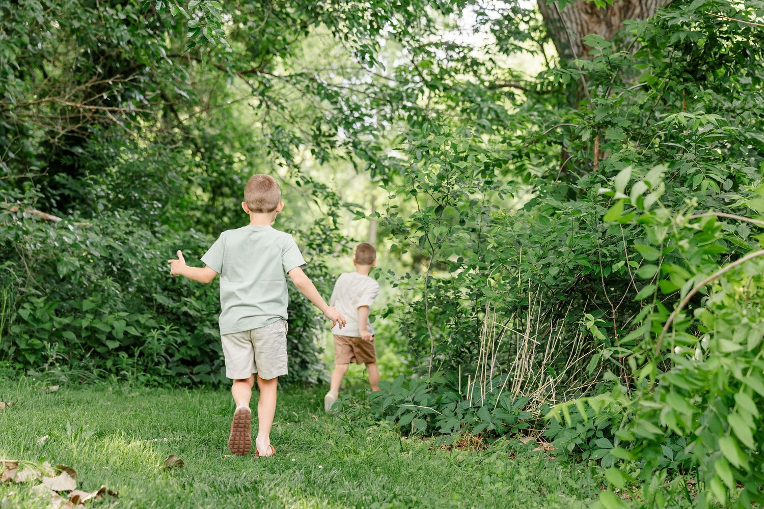 Young boy running through the trees during a playful family session at Shamrock Hills Park in Crystal Lake, Illinois.