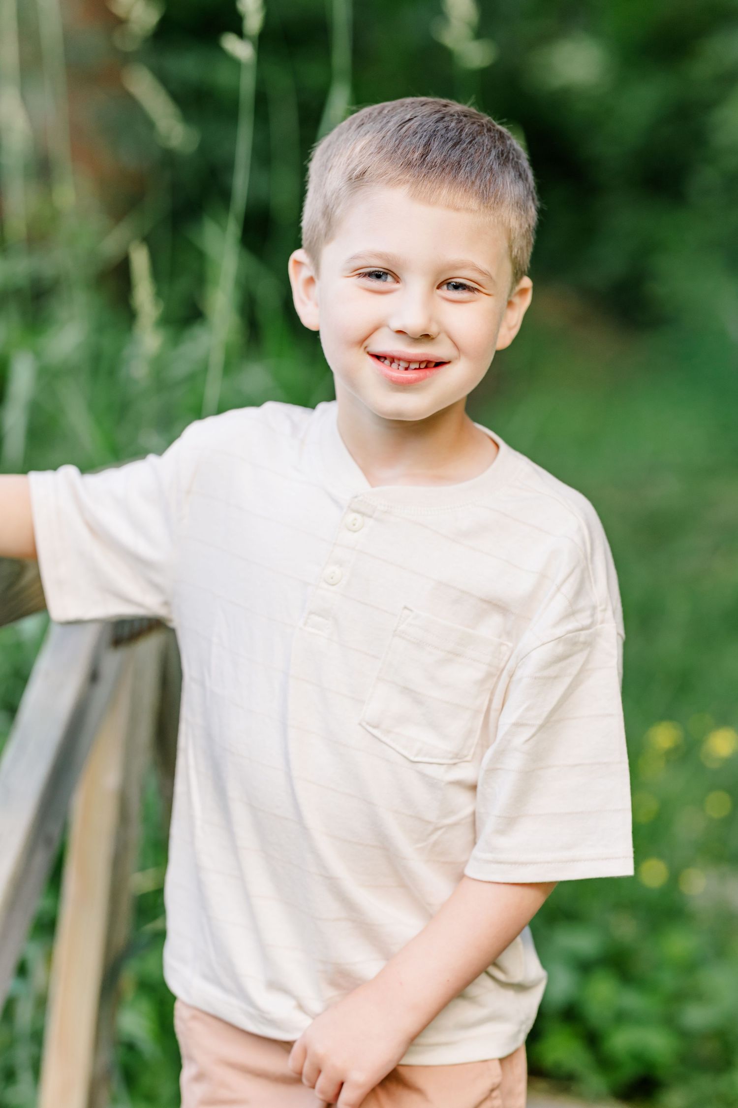 Young boy smiling near the trees during a summer family portrait session at Shamrock Hills Park in Crystal Lake.
